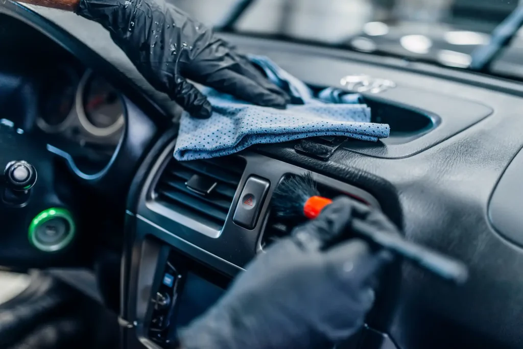Auto detailing of car interior on carwash service. Worker in gloves cleans salon with brush